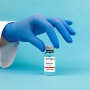 A hand in blue gloves handling a COVID-19 vaccine vial against a blue background.